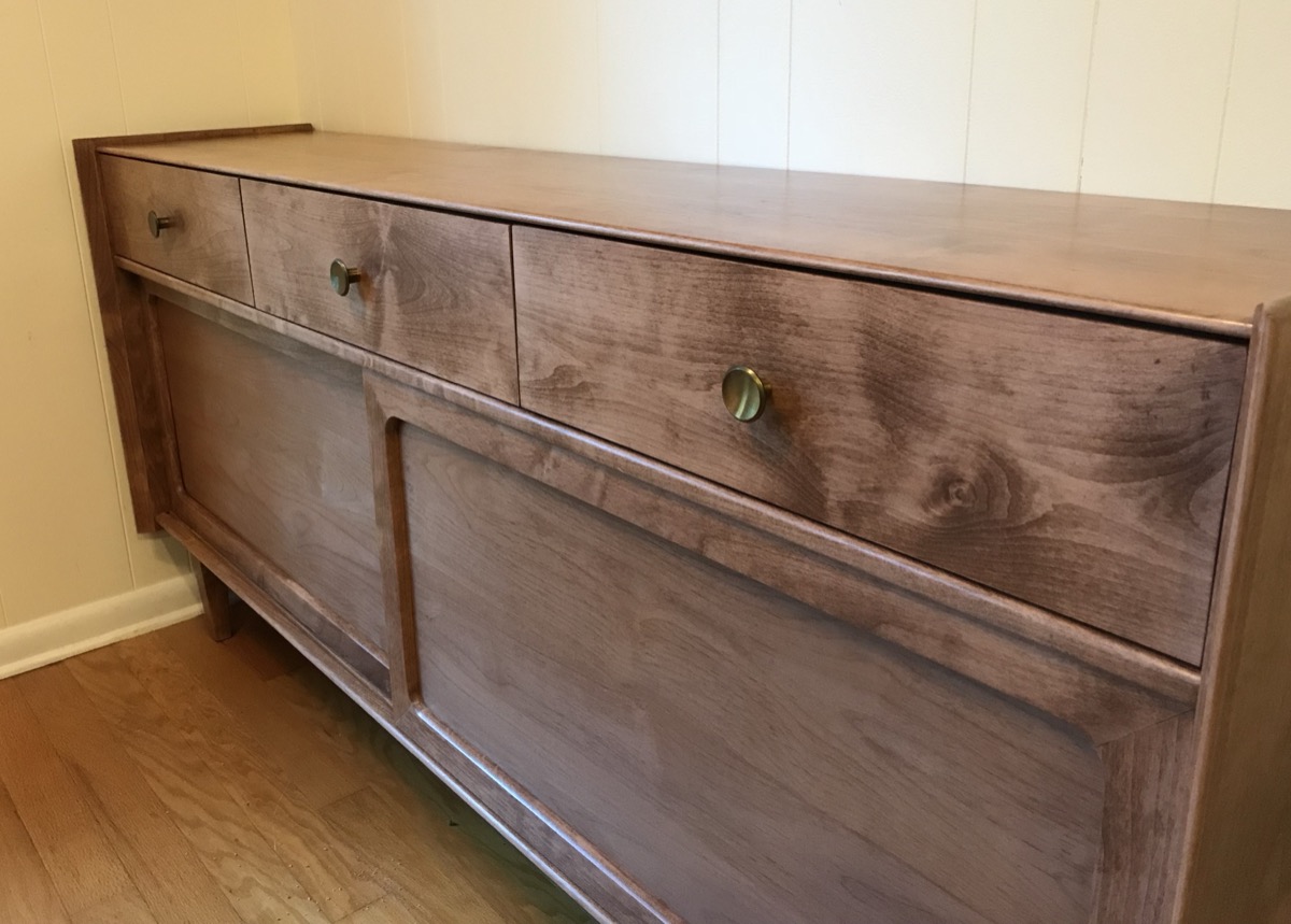 Low walnut sideboard with three top drawers, panelled cabinet doors, and round bronze pulls