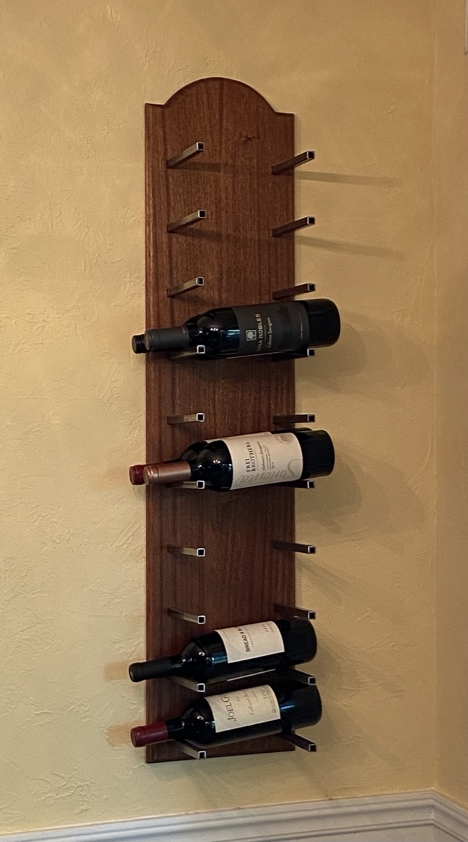 Wall-mounted walnut wine rack holding six bottles horizontally on pegs against an arched back