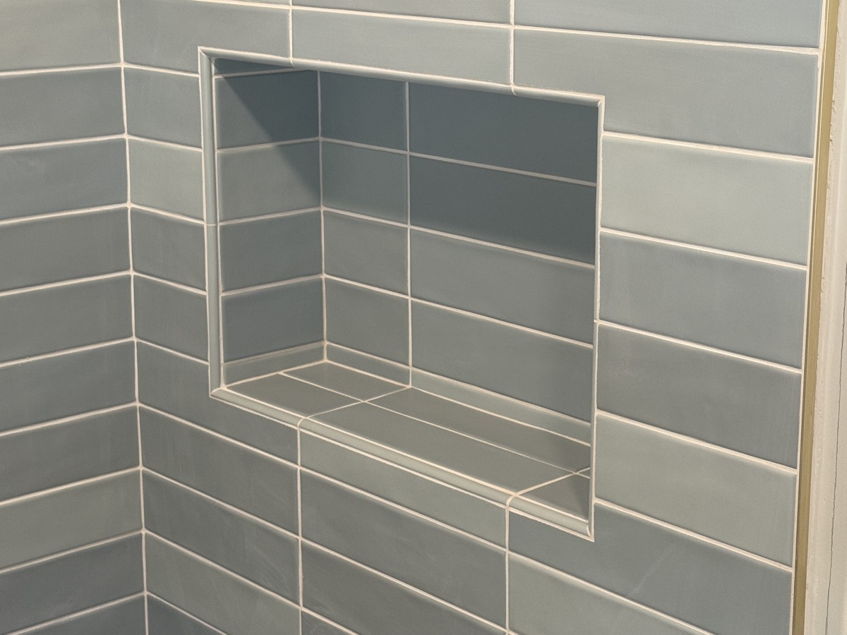 Recessed shower niche with a shelf, tiled in blue-gray stacked tile with mitered edges