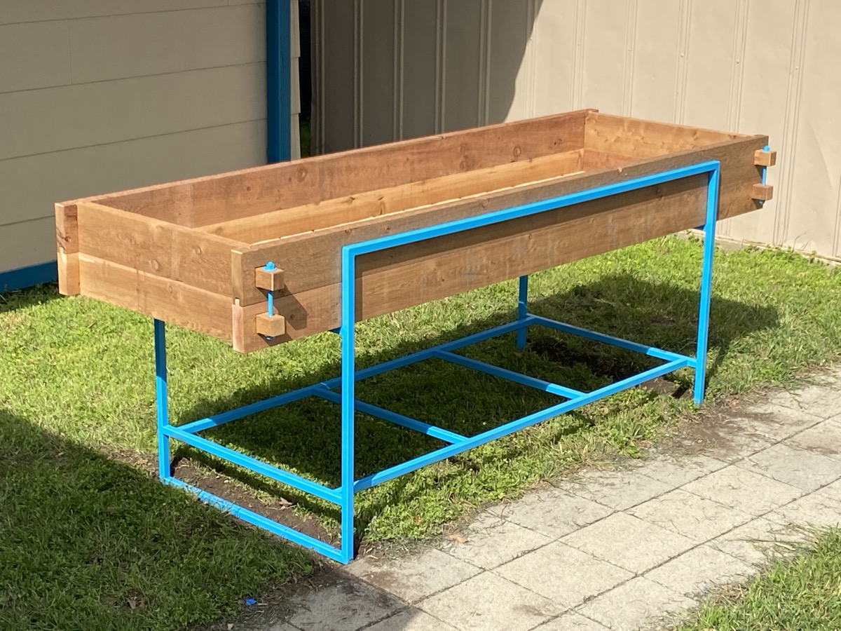 Waist-high cedar planter box mounted on a welded tubular steel frame, outdoors on grass