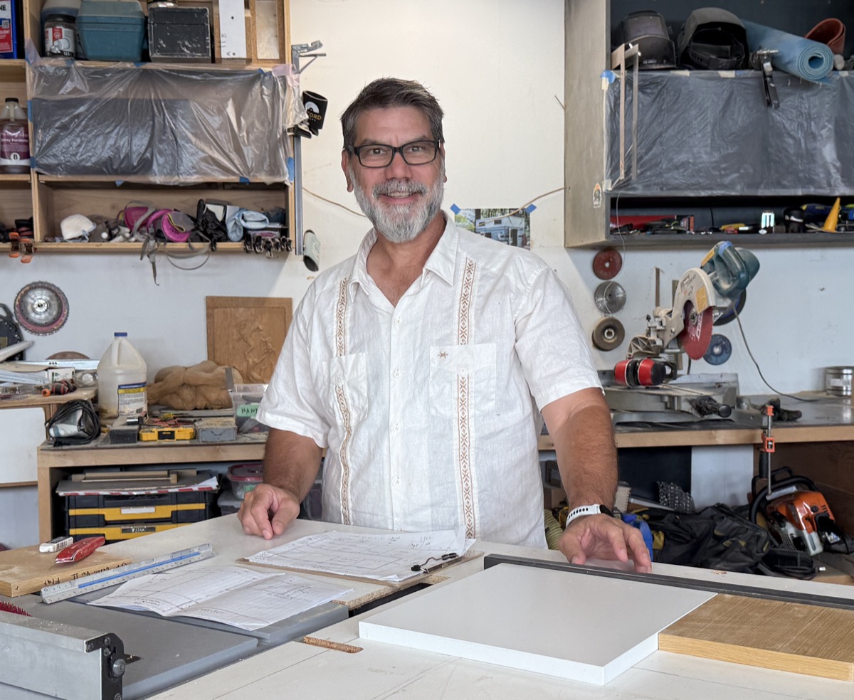 Dmitri standing at his workbench in his Austin shop, tools and materials on the wall behind him